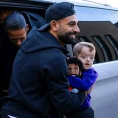 a man holding two small children in his arms as he walks out of a car