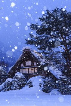 a cabin in the middle of a snowy forest with snow falling down on it's roof