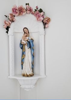 a statue of the virgin mary and child jesus on a shelf with flowers around it