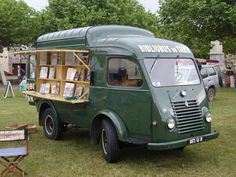 an old green truck is parked in the grass with books on it's shelf