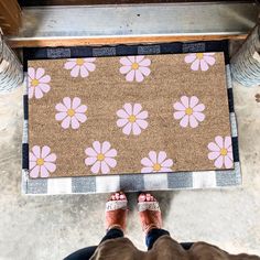 a person standing in front of a door mat with pink flowers on it and two legs