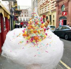 an ice cream cone covered in sprinkles and colored candies on a city street