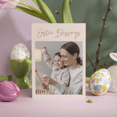 a woman holding a child in her arms next to some easter eggs and an egg decoration