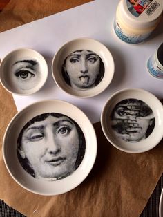 four bowls with faces painted on them are sitting on a table next to an empty bottle