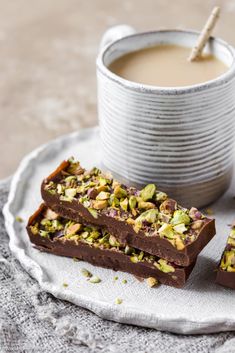 two pieces of chocolate with pistachio and nuts next to a cup of coffee