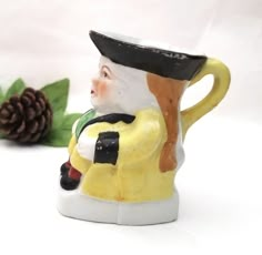 a ceramic figurine with a hat on it's head next to a pine cone