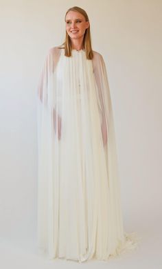 a woman wearing a white dress with sheer sleeves and an open cape over her shoulders