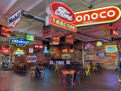 the inside of a restaurant with neon signs hanging from the ceiling and tables in front of them