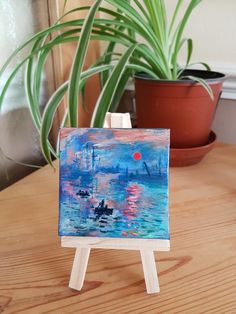 an easel sitting on top of a wooden table next to a potted plant