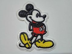 a mickey mouse iron - on patch sitting on top of a white surface with black and yellow trim