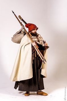 a man dressed in medieval clothing holding a long stick and bag with both hands on his hip