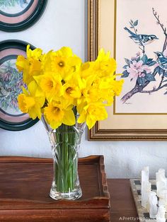 a vase filled with yellow flowers sitting on top of a wooden table next to framed pictures