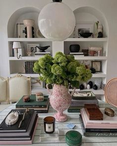 a table topped with lots of books next to a vase filled with flowers and plants