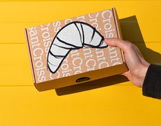 a person holding up a box with an image of a croissant on it