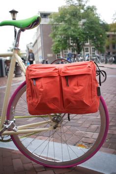 an orange bag is strapped to the back of a pink and white bicycle on a brick sidewalk