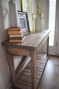 a wooden table topped with books next to a window and framed pictures on the wall