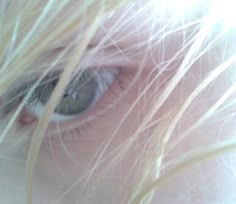 a close up view of a person's eye with long blonde hair blowing in the wind