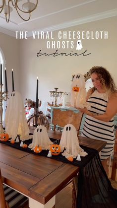 a woman standing in front of a table with ghost decorations on it and candles behind her