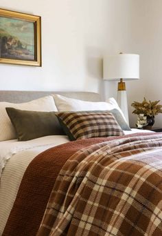 a bed with plaid comforter and pillows in a bedroom next to a painting on the wall