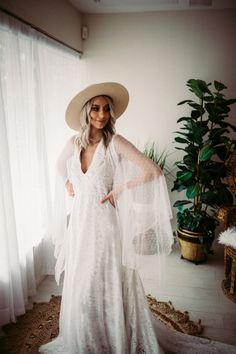 a woman in a white dress and hat standing by a window with her hands on her hips