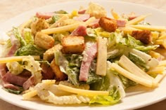 a salad with cheese, lettuce and ham on it sitting on a white plate