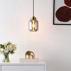 a vase with white flowers on a table next to a light fixture and framed pictures