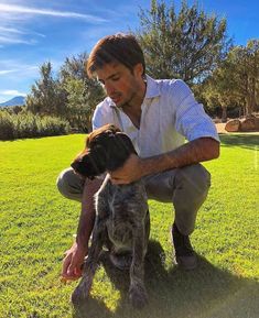 a man kneeling down petting a dog in the grass