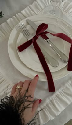 a woman is setting the table with silverware and red ribbon on it's edge