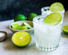 two margaritas with lime slices and sugar on the rim, next to bowls of limes