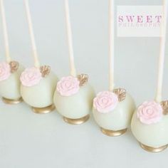 white cake pops with pink flowers on them are lined up in gold and silver holders