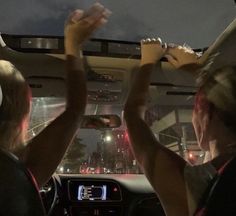 two women are sitting in the back seat of a car and one is holding her hand up