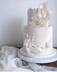 a three tiered white wedding cake sitting on top of a table next to a cloth