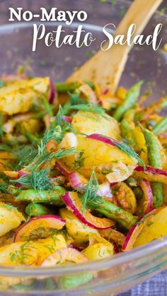 a salad with potatoes and green beans in a glass bowl next to a wooden spoon