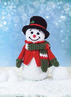 a crocheted snowman wearing a red scarf and black hat, standing in the snow