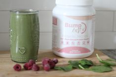 a green smoothie next to a jar of powdered protein and raspberries