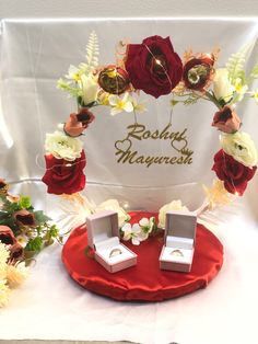 two wedding rings are sitting on a red table with flowers and greenery around them