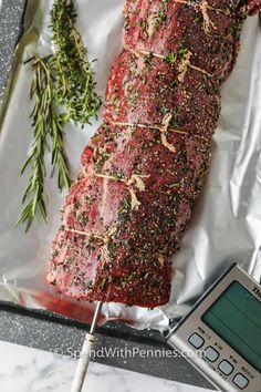 a piece of meat is being weighed on a table with a digital scale and rosemary sprigs