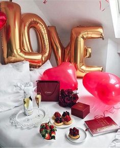 a table topped with lots of balloons and desserts next to a large love balloon