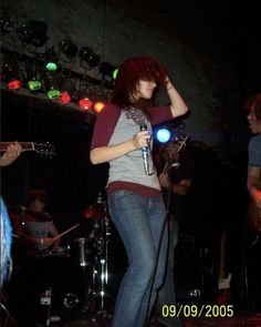 a woman singing into a microphone while standing next to other people playing instruments in the background