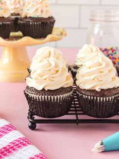 chocolate cupcakes with white frosting and sprinkles on a pink table