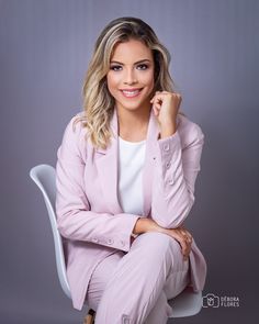 a woman sitting on top of a white chair wearing a pink suit and smiling at the camera