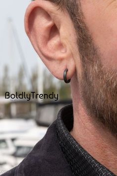 the man is wearing his ear piercings and looking into the distance with boats in the background