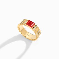 a yellow gold ring with red stone and white diamonds on the sides, against a white background