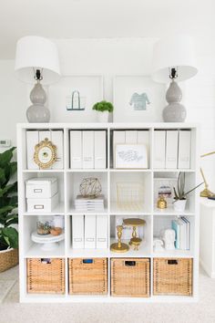 a white bookcase filled with lots of boxes and baskets next to two lamps on top of each shelf