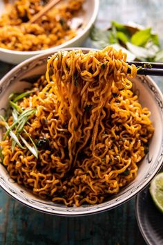 a bowl filled with noodles and chopsticks on top of a table next to lime slices