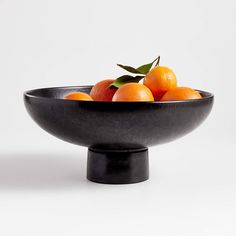 a black bowl filled with oranges on top of a table