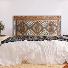 a bed with white sheets and a wooden headboard on top of it, next to a potted plant