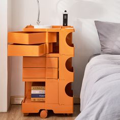 an orange shelf next to a bed with a lamp on top of it in a bedroom