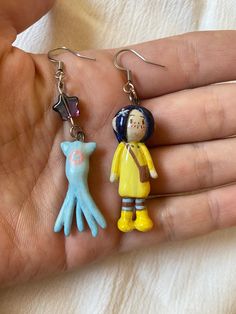 a person is holding two small items in their hand while wearing earrings that look like little people