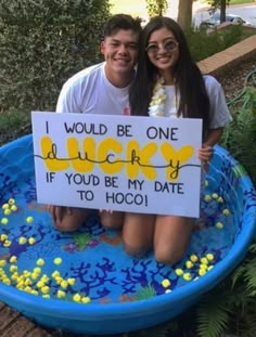 two people sitting in a pool holding a sign that says i would be one lucky if you be my date to hoo